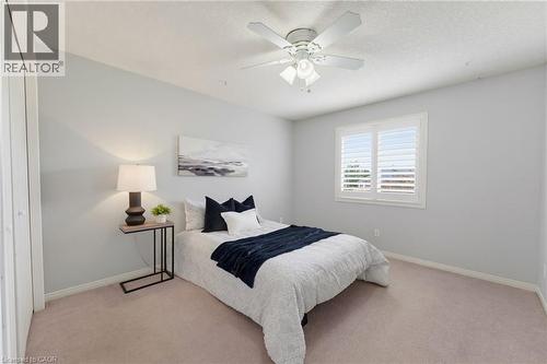 Angled ceiling line, ceiling fan with integrated lighting, window with plantation shutters, light-toned carpet, and a light-colored wall finish - 592 Little Dover Crescent, Waterloo, ON - Indoor Photo Showing Bedroom