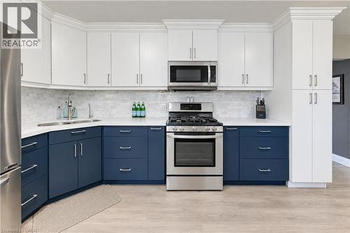 Two-tone cabinetry with white upper and blue lower cabinets, stainless steel appliances, white countertop, white subway tile backsplash, and wood-finish flooring - 87 Bond Street, Kitchener, ON 