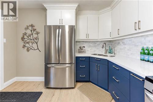Stainless steel refrigerator, dual-tone cabinetry, white countertops, tile backsplash, and wood-finish flooring - 87 Bond Street, Kitchener, ON 