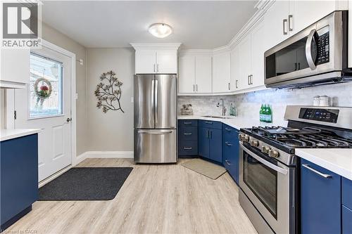 Two-tone cabinetry with white upper and blue lower units, stainless steel appliances, marble tile backsplash, solid surface countertops, and wood-finish flooring - 87 Bond Street, Kitchener, ON 