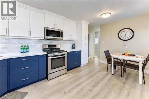 Two-tone cabinetry with white upper and blue lower cabinets, stainless steel appliances, white countertops, and wood-finish flooring - 87 Bond Street, Kitchener, ON 