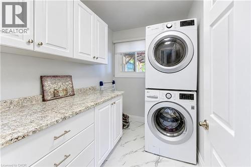 White shaker cabinetry, light-toned countertop, stacked laundry appliances, white panel door, and a single window - 87 Bond Street, Kitchener, ON 