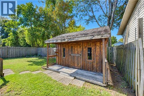 Detached shed with wood siding and covered porch, featuring a wooden privacy fence, established trees, and a grassy yard - 87 Bond Street, Kitchener, ON 
