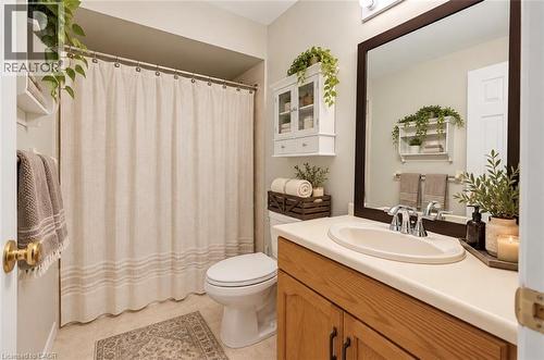 Recessed shower/tub combination, single-sink vanity with wood-finish cabinetry, solid surface countertop, and framed mirror - 56 Windrush Trail, Kitchener, ON 