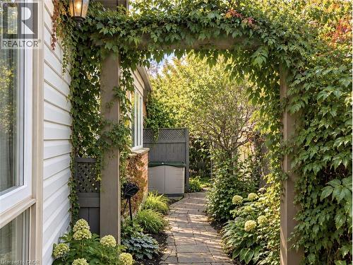 Arbor entryway with climbing vines, paver pathway, mature plantings, and exterior wall lighting - 56 Windrush Trail, Kitchener, ON 