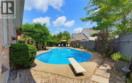 Curved in-ground pool with concrete surround, diving board, and stone paver patio - 56 Windrush Trail, Kitchener, ON 