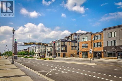 Modern streetscape featuring mixed-use buildings with brick and paneling facades, commercial storefronts, and a decorative overhead archway - 65 Waterview Lane, Grimsby, ON 