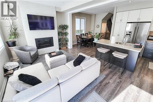 Open-concept living area featuring wood-finish flooring, a contemporary fireplace with a textured surround, and a kitchen island with seating - 65 Waterview Lane, Grimsby, ON 
