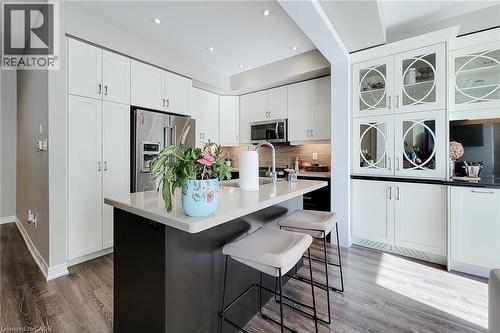 Modern kitchen featuring abundant white cabinetry, stainless steel appliances, a center island with countertop seating, and wood-finish flooring - 65 Waterview Lane, Grimsby, ON 