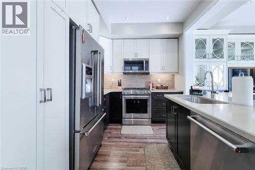 Stainless steel appliances, white and dark wood-finish cabinetry, light-toned countertops, tile backsplash, and wood-finish flooring - 65 Waterview Lane, Grimsby, ON 