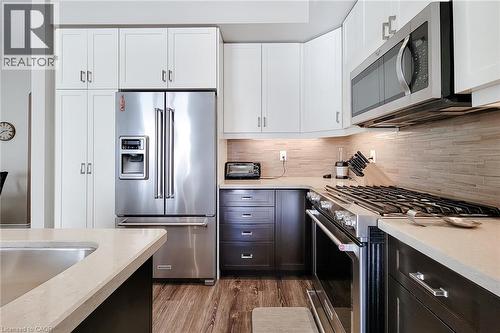 Stainless steel appliances, wood-finish flooring, white upper cabinetry, dark lower cabinetry, and light-toned countertops - 65 Waterview Lane, Grimsby, ON 