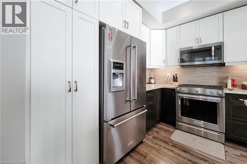 Stainless steel appliances, wood-finish flooring, two-tone cabinetry, light-toned backsplash, and white countertops - 65 Waterview Lane, Grimsby, ON 