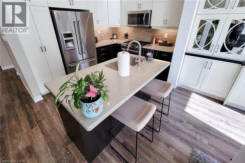 Stainless steel refrigerator, stainless steel microwave, stone countertops, two-tone cabinetry, and wood-finish flooring - 65 Waterview Lane, Grimsby, ON 