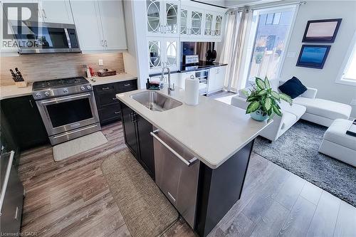 Kitchen island with integrated sink, stainless steel appliances, and wood-finish flooring - 65 Waterview Lane, Grimsby, ON 
