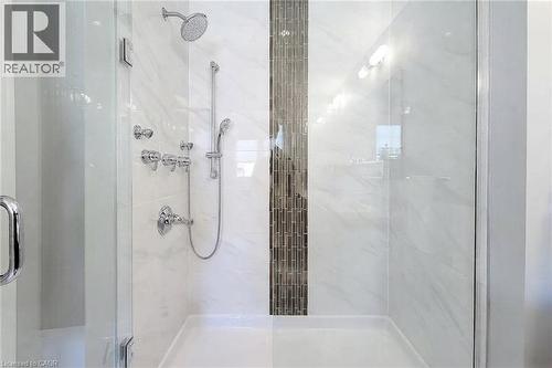 Glass-enclosed shower with a rainfall showerhead, handheld sprayer, multiple body jets, and a decorative tile accent band - 65 Waterview Lane, Grimsby, ON 