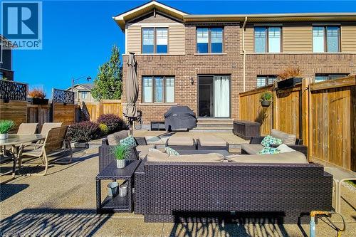 Expansive stone patio with a brick and siding exterior, featuring a sliding glass door and fenced perimeter - 65 Waterview Lane, Grimsby, ON 