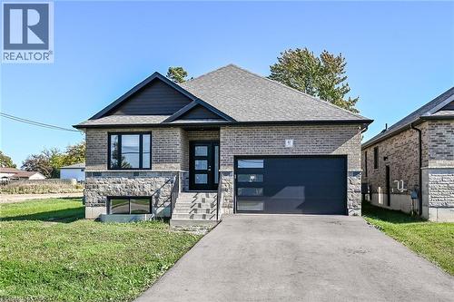 Contemporary exterior with a dark gray shingle roof, light brick siding, stone facade, and a modern garage door with frosted glass panels - 41 Eleanor Avenue, Hamilton, ON 