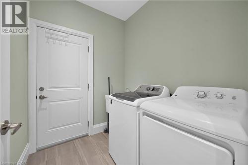 Laundry area featuring light green walls, a white paneled door with brushed nickel hardware, and wood-finish flooring - 41 Eleanor Avenue, Hamilton, ON 
