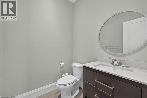 Vanity with integrated sink, stone countertop, wood-finish cabinetry, and a circular wall mirror - 41 Eleanor Avenue, Hamilton, ON 