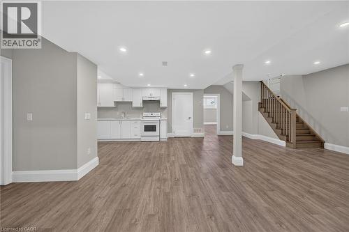 Open-concept area featuring wood-finish flooring, recessed lighting, a full kitchen with white cabinetry and appliances, and a wood staircase - 41 Eleanor Avenue, Hamilton, ON 