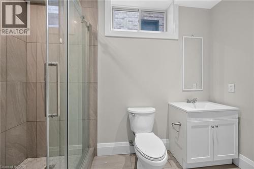 Shower with tile surround and glass enclosure, white vanity with integrated sink, white toilet, and tile flooring - 41 Eleanor Avenue, Hamilton, ON 