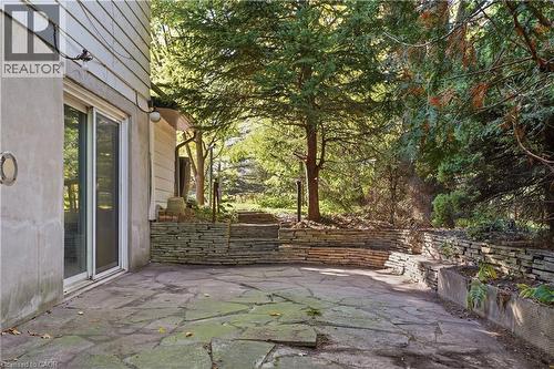Stone patio with irregular flagstone paving, multiple stacked stone retaining walls, and mature trees - 12 Hill Street, Kitchener, ON 