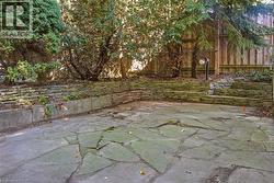 Stone patio with a tiered retaining wall, integrated planter, and mature perimeter trees - 
