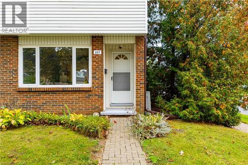 Exterior facade featuring a combination of red brick and white horizontal siding, a multi-pane fixed window, a white entry door with an arched glass insert, and a brick paver walkway - 227 Fergus Avenue, Kitchener, ON 