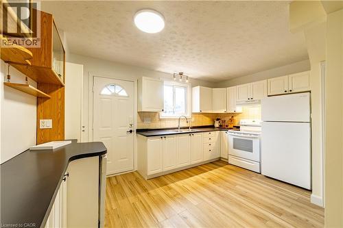 Kitchen featuring white shaker-style cabinetry, dark solid-surface countertops, wood-finish flooring, and built-in task lighting - 227 Fergus Avenue, Kitchener, ON 