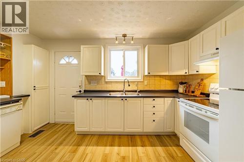 Kitchen featuring white shaker-style cabinetry, dark solid-surface countertops, tile backsplash, stainless steel dual-basin sink, and wood-finish flooring - 227 Fergus Avenue, Kitchener, ON 