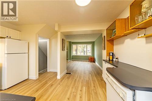Kitchen featuring wood-finish flooring, white cabinetry, dark countertops, built-in upper shelving, and a large multi-pane window - 227 Fergus Avenue, Kitchener, ON 