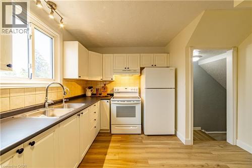 Kitchen featuring white cabinetry, wood-finish flooring, tiled backsplash, dual-basin stainless steel sink, and white appliances - 227 Fergus Avenue, Kitchener, ON 