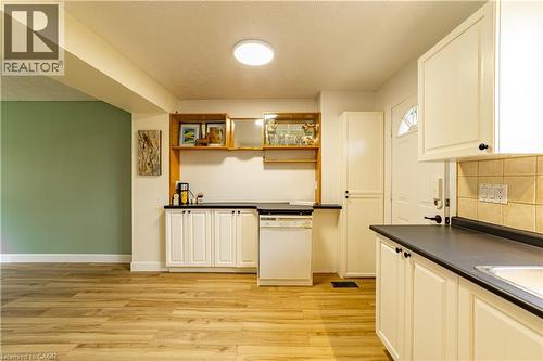 Kitchen featuring white shaker-style cabinetry, dark contrast countertops, wood-finish flooring, built-in display shelving, and an integrated dishwasher - 227 Fergus Avenue, Kitchener, ON 