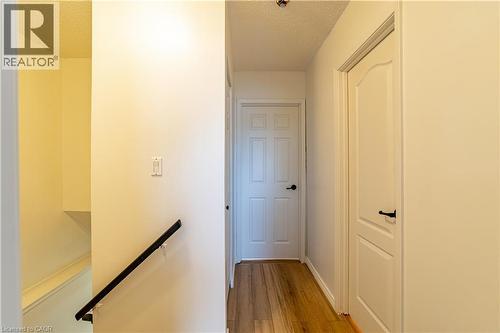 Hallway featuring wood-finish flooring, two-panel interior doors, and a matte black wall-mounted handrail - 227 Fergus Avenue, Kitchener, ON 