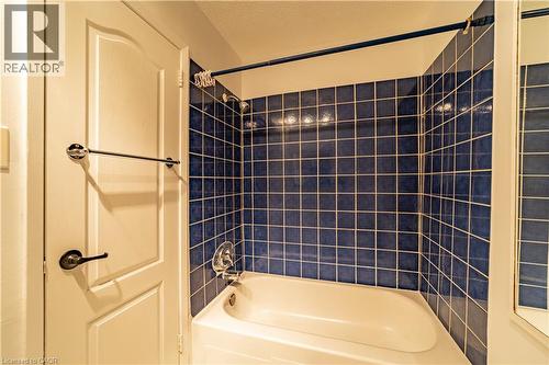 Bathtub featuring a deep-blue tiled surround, chrome shower head and faucet hardware, and a matching chrome towel bar - 227 Fergus Avenue, Kitchener, ON 