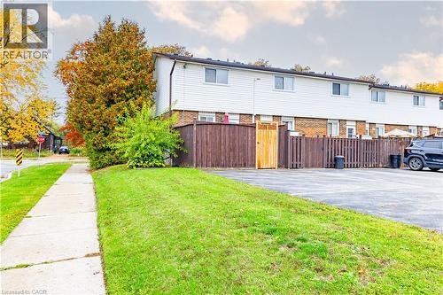 Multi-level exterior featuring horizontal siding, brick masonry foundation, private wood-fenced enclosure, and an asphalt parking area - 227 Fergus Avenue, Kitchener, ON 