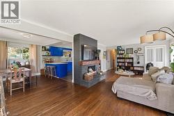 Open-concept living area featuring rich wood-finish flooring, a painted brick fireplace with a wood mantle, and bright blue kitchen cabinetry - 