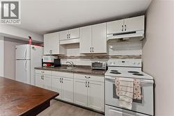 White cabinetry with dark hardware, a subway tile backsplash, and wood-finish flooring - 