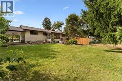 Expansive lawn area with mature trees, offering a covered patio space and partial wood fencing - 