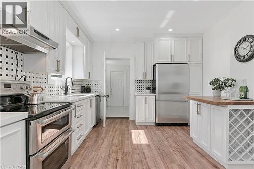 Kitchen featuring white cabinetry, stainless steel appliances, wood-finish flooring, a patterned tile backsplash, and a built-in wine rack - 164 Wilson Street, Hamilton, ON 