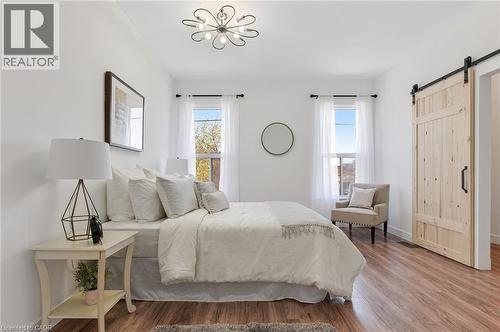 Wood-finish flooring, two windows with white curtains, white walls, and a light wood-tone barn door with black hardware - 164 Wilson Street, Hamilton, ON 