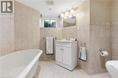 Spa-inspired bathroom featuring a freestanding soaking tub, tile surround, vanity with dual cabinet storage, vessel sink, polished chrome fixtures, and pendant lighting above the mirror - 164 Wilson Street, Hamilton, ON 