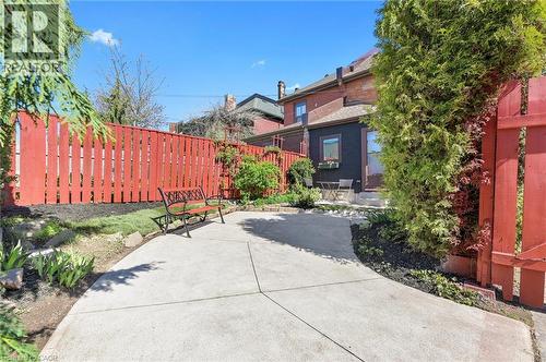 Private backyard oasis featuring a concrete patio, mature ivy-covered perimeter fencing in vibrant red, lush green landscaping, and a black metal bench - 164 Wilson Street, Hamilton, ON 