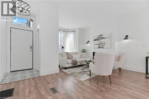 Bright open-concept living area featuring wood-finish flooring throughout, white shaker-style entry door with transom window, recessed ceiling lighting, and contemporary wall-mounted sconces - 164 Wilson Street, Hamilton, ON 