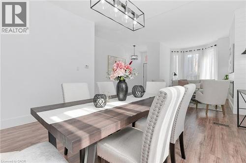 Sophisticated dining space showcasing a wood-finish table with geometric base, paired with upholstered dining chairs featuring nailhead trim - 164 Wilson Street, Hamilton, ON 