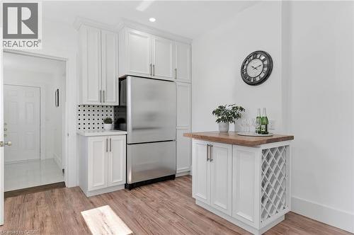 White shaker cabinetry, stainless steel refrigerator, patterned tile backsplash, wood-finish flooring, and a built-in wine rack - 164 Wilson Street, Hamilton, ON 