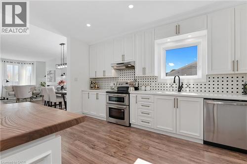 Contemporary kitchen featuring white shaker-style cabinetry, stainless steel appliances including double wall ovens and dishwasher, polished black countertops, geometric tile backsplash, and brushed n - 164 Wilson Street, Hamilton, ON 