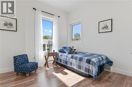 Bright secondary bedroom showcasing wood-finish flooring, dual windows with natural light exposure, and clean white walls - 164 Wilson Street, Hamilton, ON 