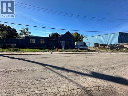 Single-story structure featuring dark-toned siding and a gable roofline, set on a corner lot with metal perimeter fencing - 150 Princess Street, Hamilton, ON 