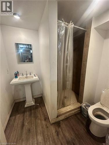 Bathroom featuring a white pedestal sink, wood-finish flooring, a wall-mounted rectangular mirror, and a tiled shower enclosure - 150 Princess Street, Hamilton, ON 